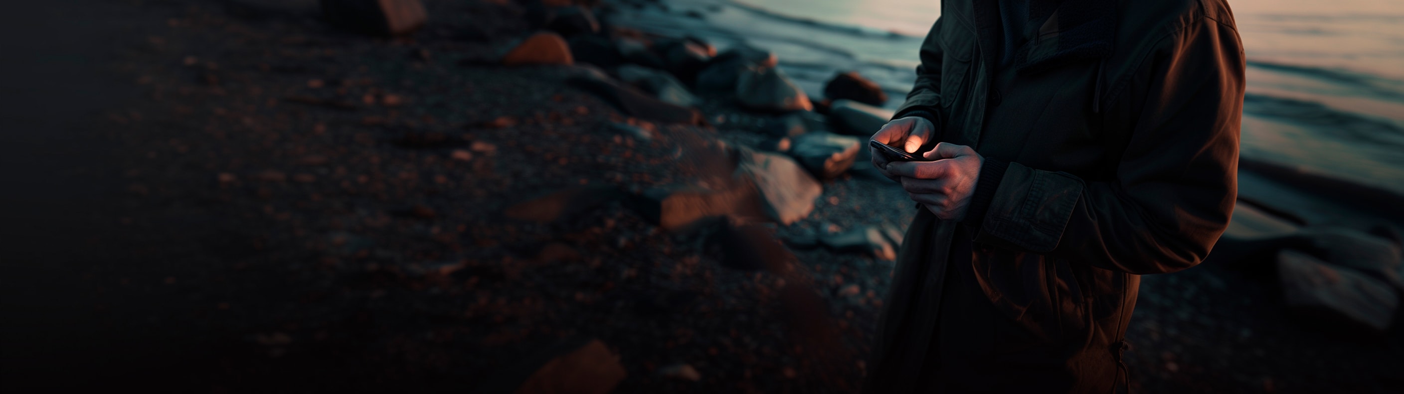Persona usando un smartphone junto al mar al atardecer, resaltando la conectividad y tecnología de CUPRA.
