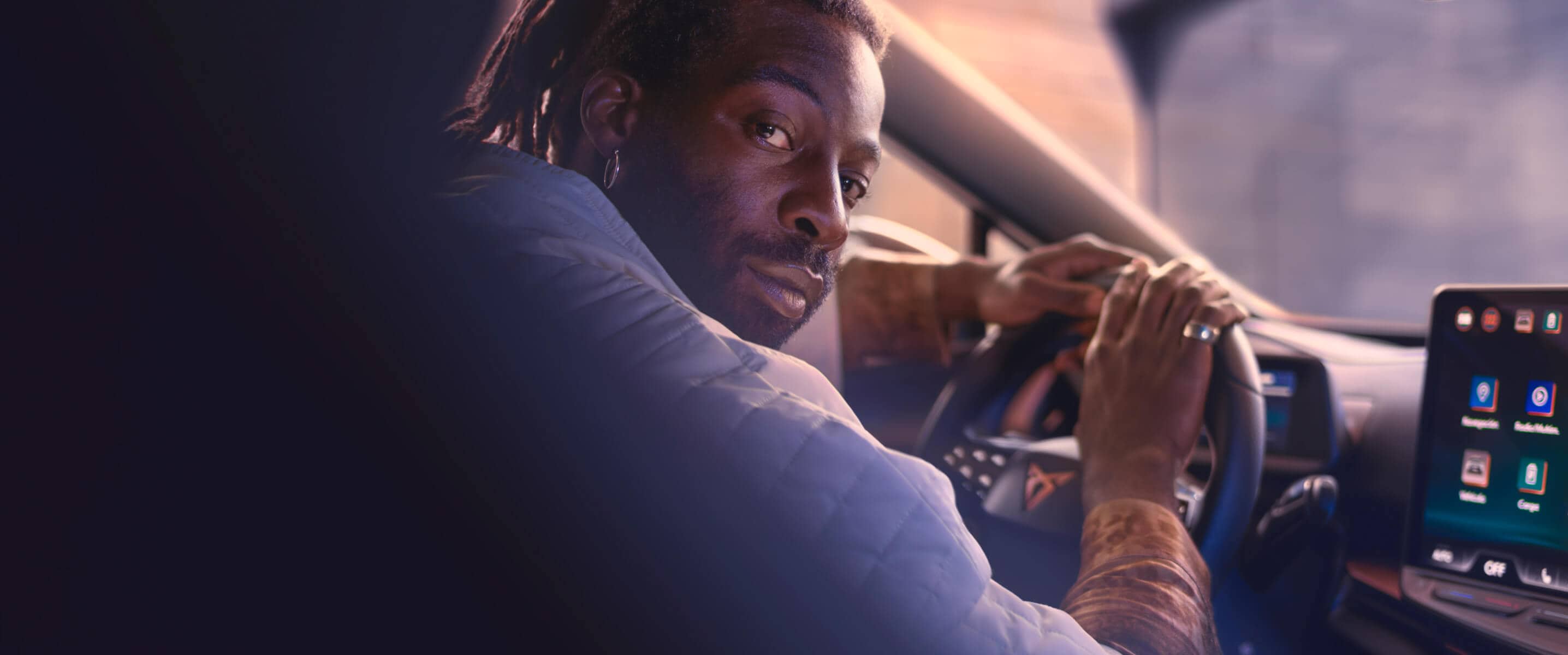 Un hombre sentado frente al volante de un coche eléctrico, conduciéndolo y mirando a un lado.
